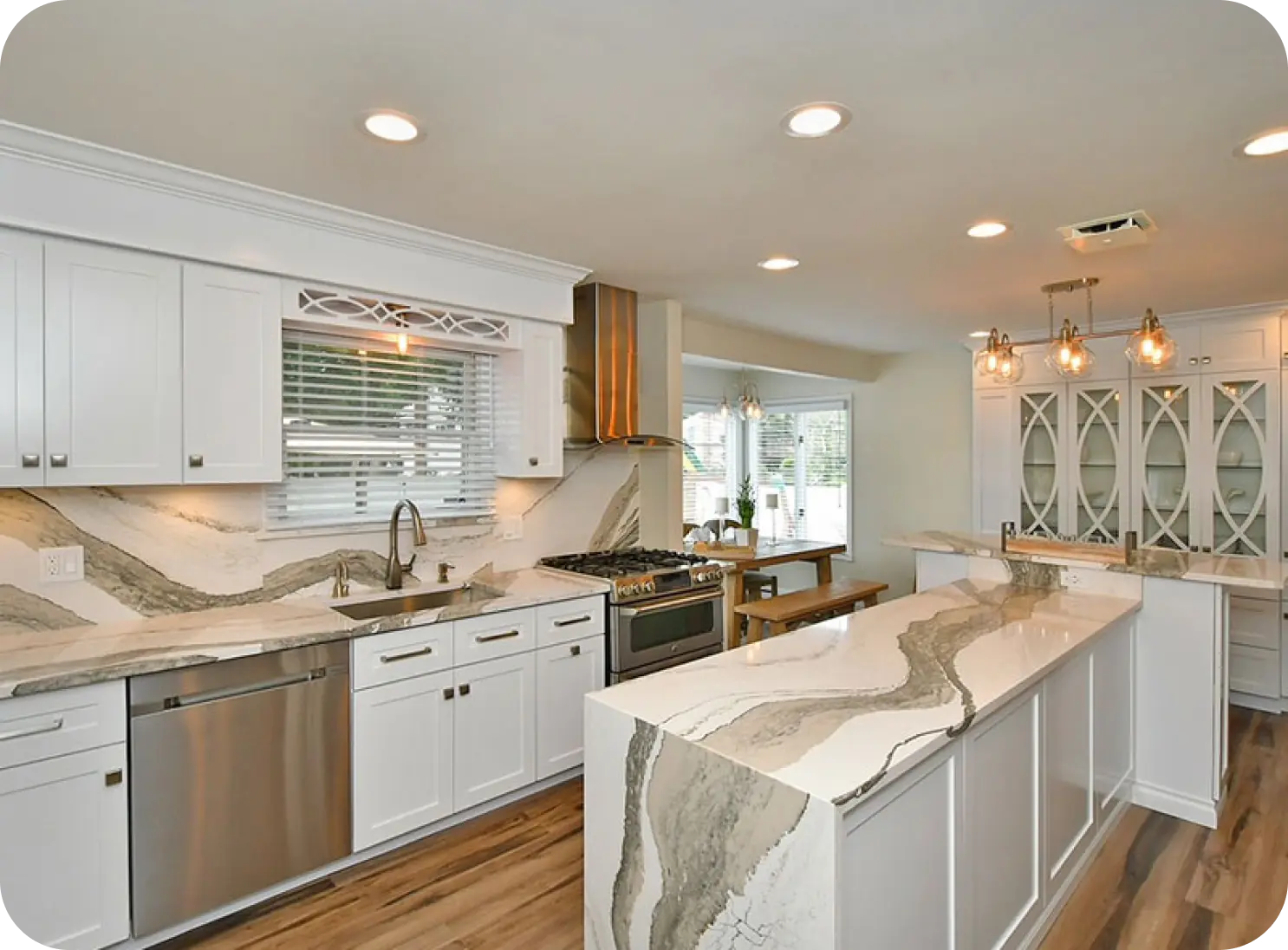 Modern kitchen with white cabinets, marble countertops, island with seating, stainless steel appliances, and wooden flooring.