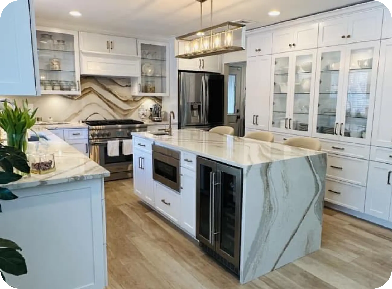 Modern kitchen with white cabinetry, a large marble island with built-in wine cooler, and stainless steel appliances. Wooden flooring and overhead lighting enhance the decor.