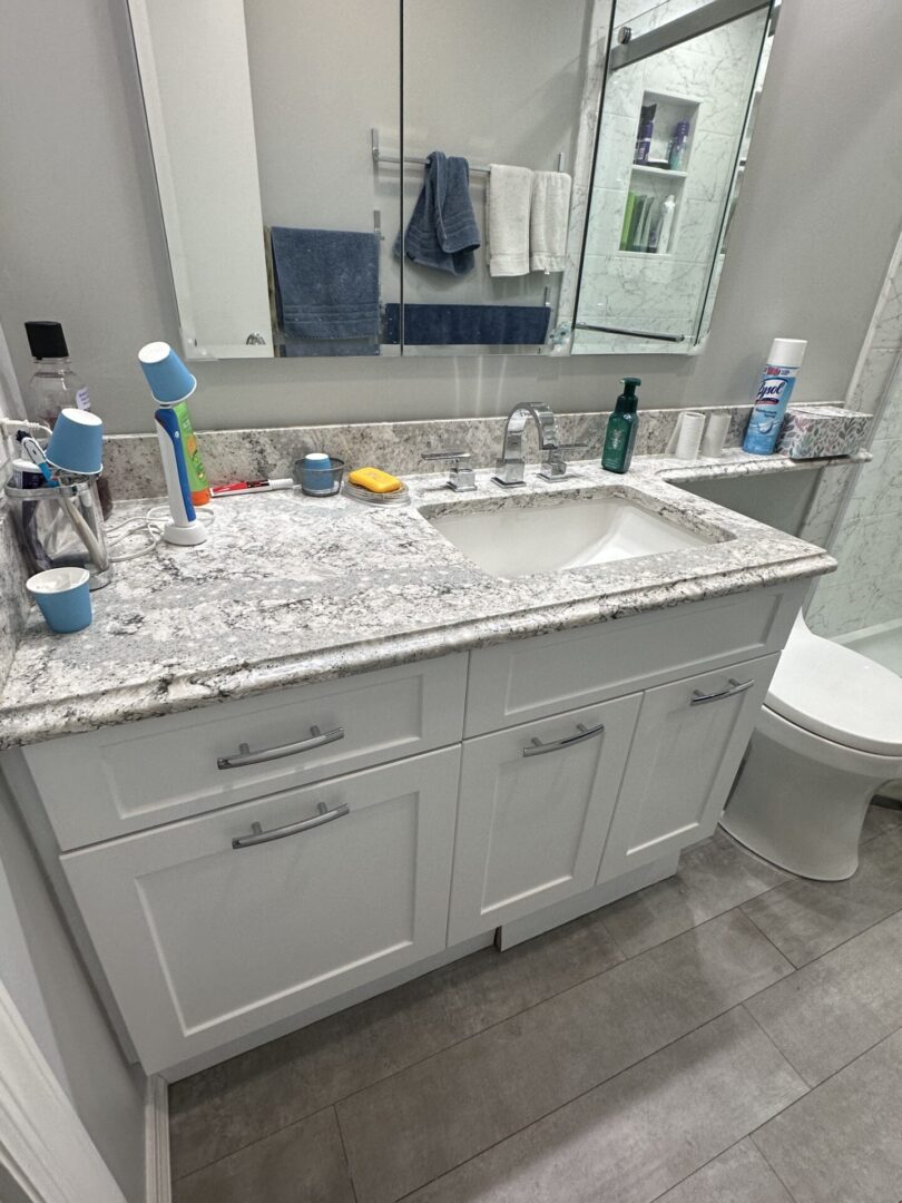 A bathroom with white cabinets and marble counter tops.