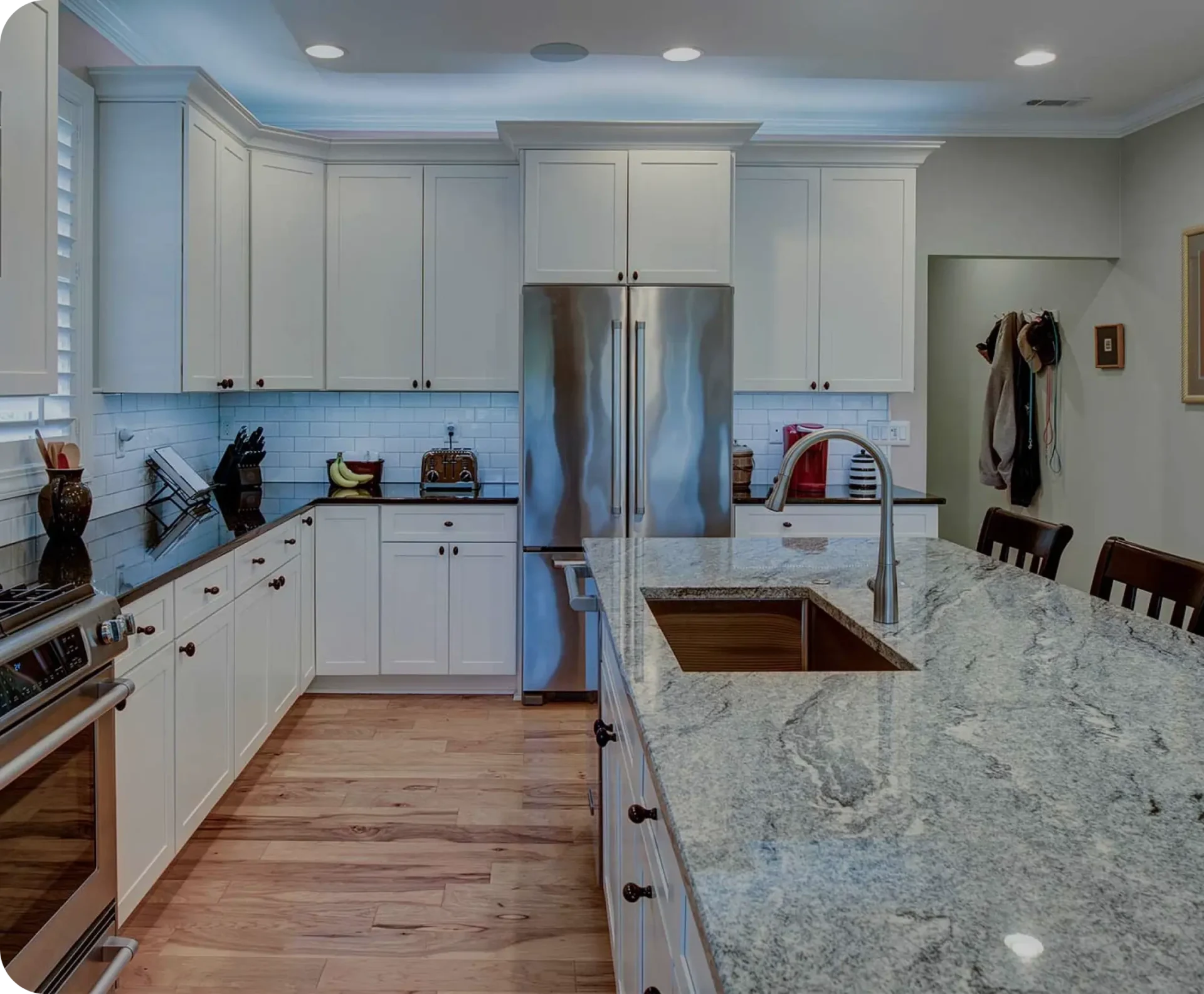 Modern kitchen with white cabinets, stainless steel appliances, and a large granite island. A coat rack is visible in the corner near the door.