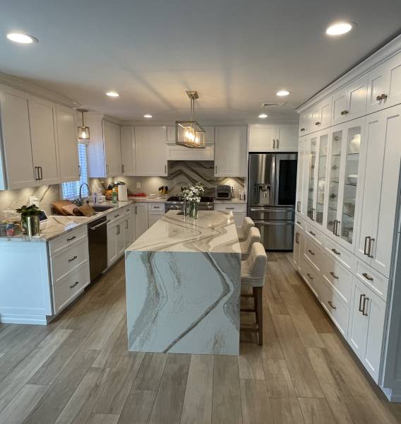 A kitchen with white cabinets and marble counter tops.