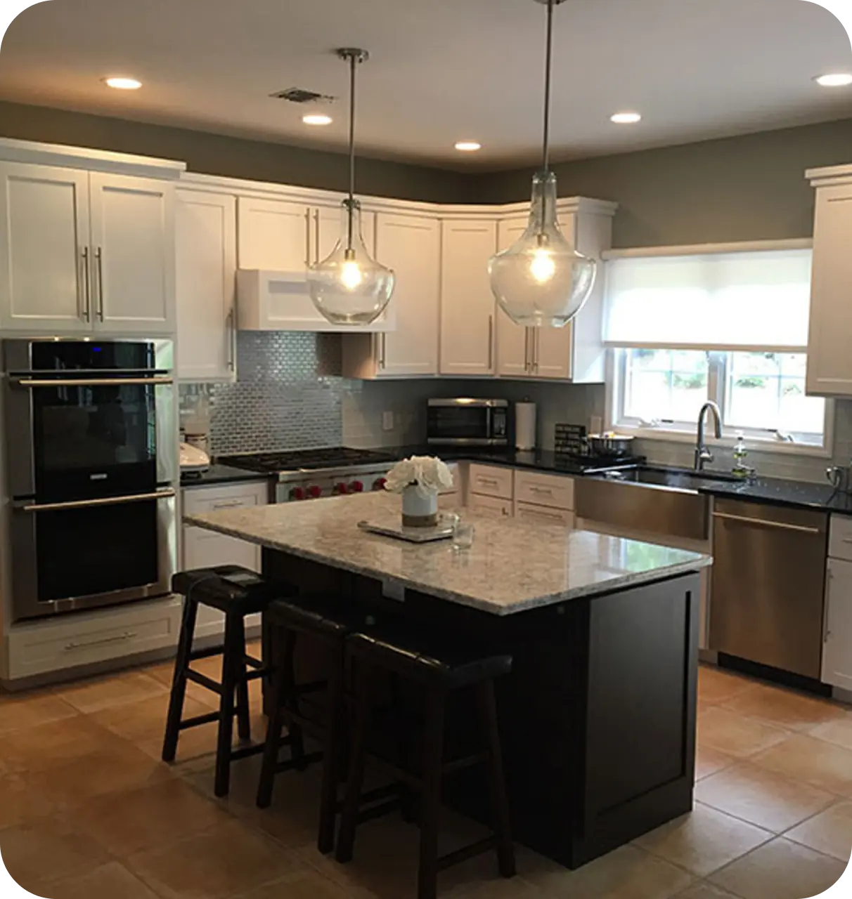 Modern kitchen with white cabinets, a black island with granite countertop, stainless steel appliances, and two pendant lights above the island.